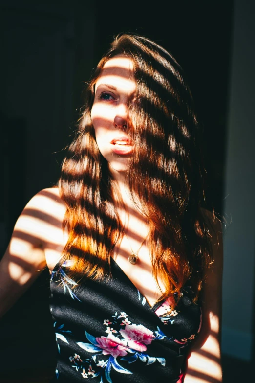 woman in floral dress standing in sunlight through window