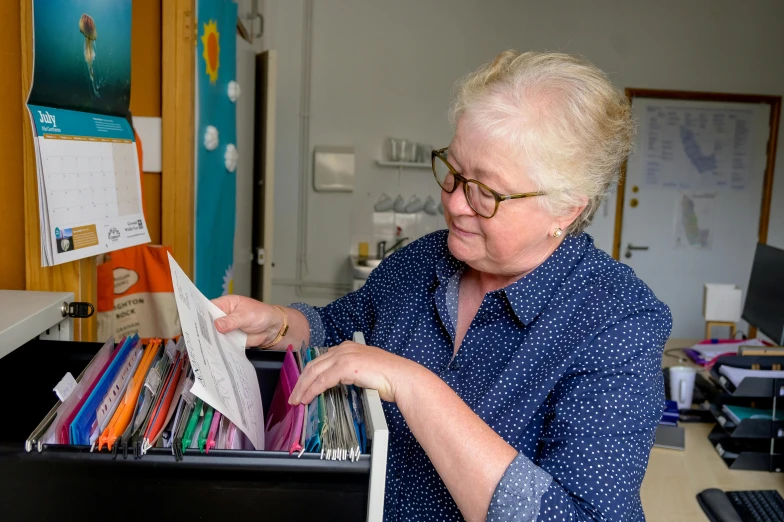 an old woman sitting at her desk picking up a folder