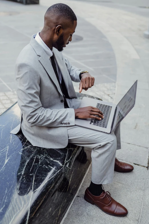 a black man in a gray suit uses his laptop