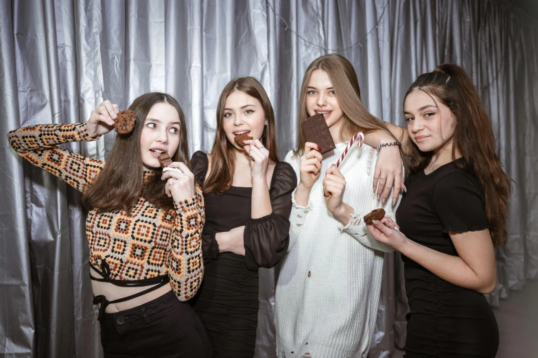 four beautiful young ladies posing in front of a silver curtain