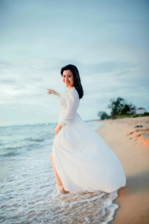 a woman in white dress standing on beach next to water