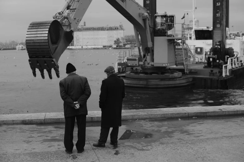 two people standing on a pier looking at a construction machine