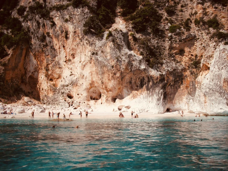 many people swimming and playing in the water near a mountain side