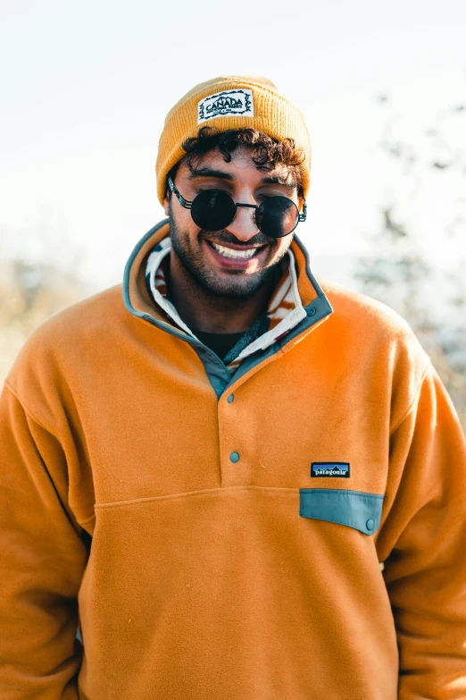 the man with his eyes closed wears sunglasses and an orange coat