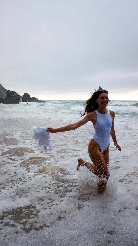 a woman running in the ocean holding her white shirt