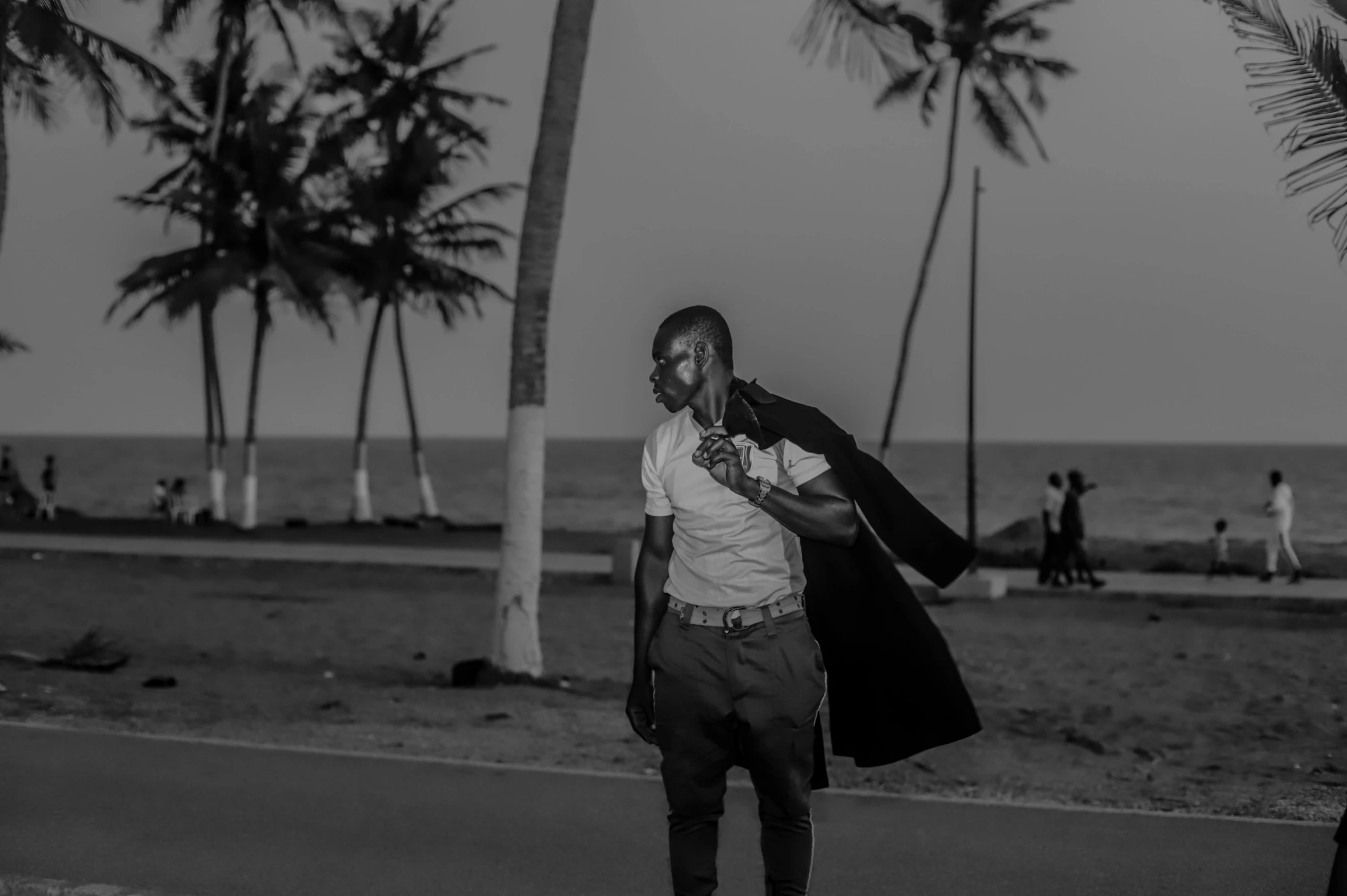 a man in white shirt and black jacket standing near palm trees