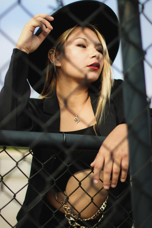 a woman wearing a hat leaning against a fence