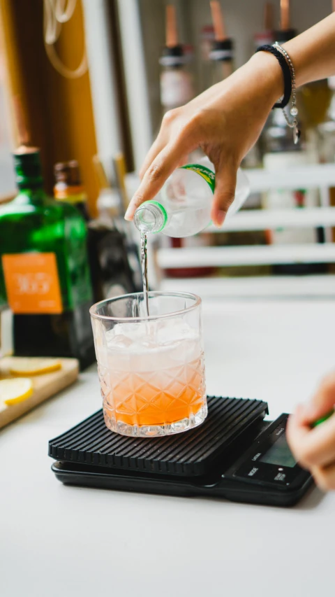 someone adding an orange wedge into a glass of liquid