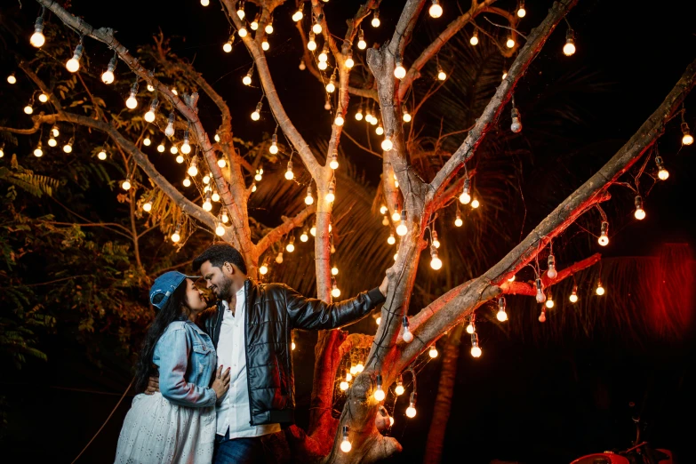 a man and woman standing next to each other under a tree with christmas lights