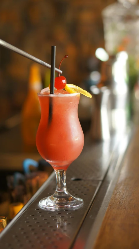 a red cocktail with a pineapple slice is on a bar