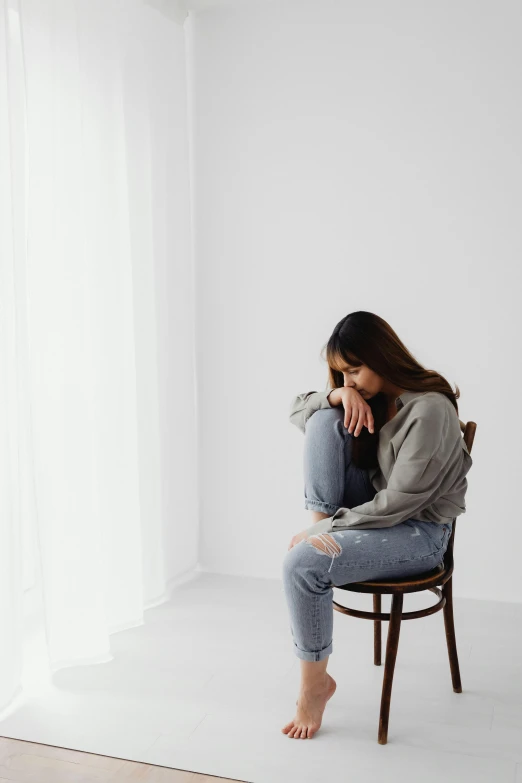 a woman in a gray sweater and jeans sitting on a chair looking at her cell phone