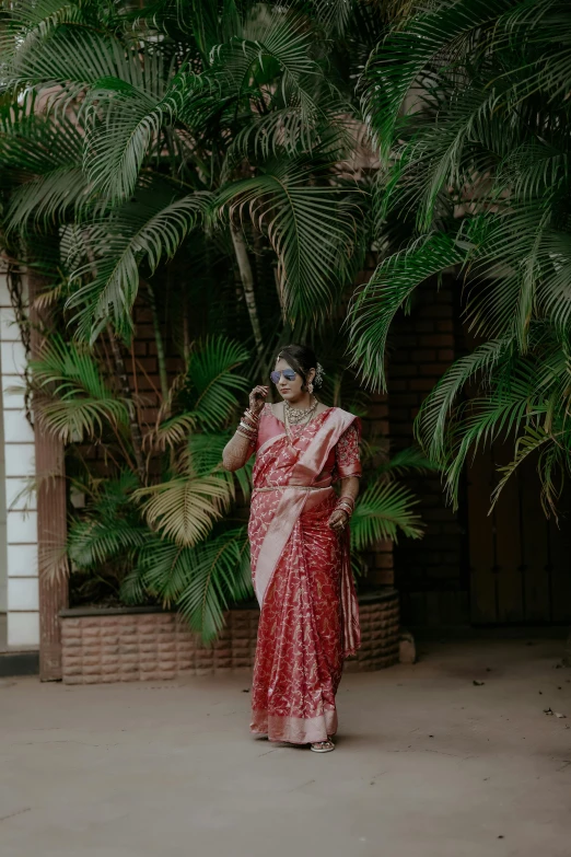 a woman in a red saree standing under some palm trees