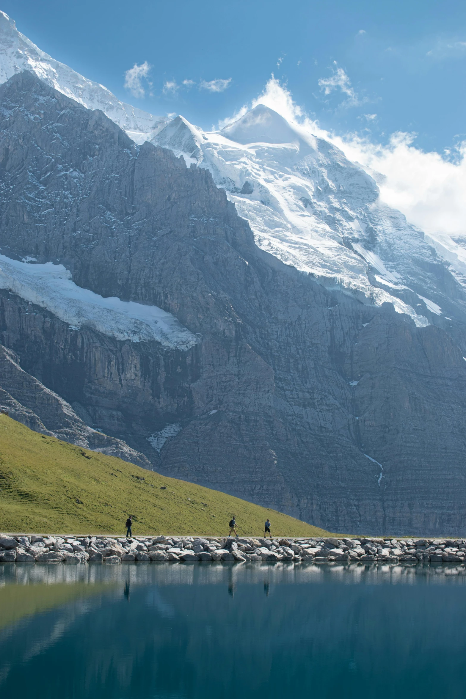 several people walking by a mountain lake with mountains in the background