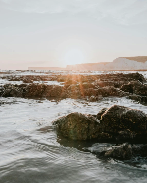 a person on an orange surfboard standing in the water at a rocky shore