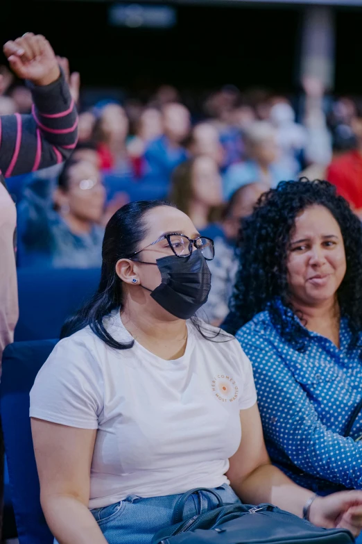 a crowd wearing a face mask while sitting in blue chairs