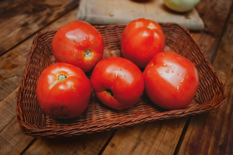 a brown basket holding many ripe tomatoes on top of a wooden table