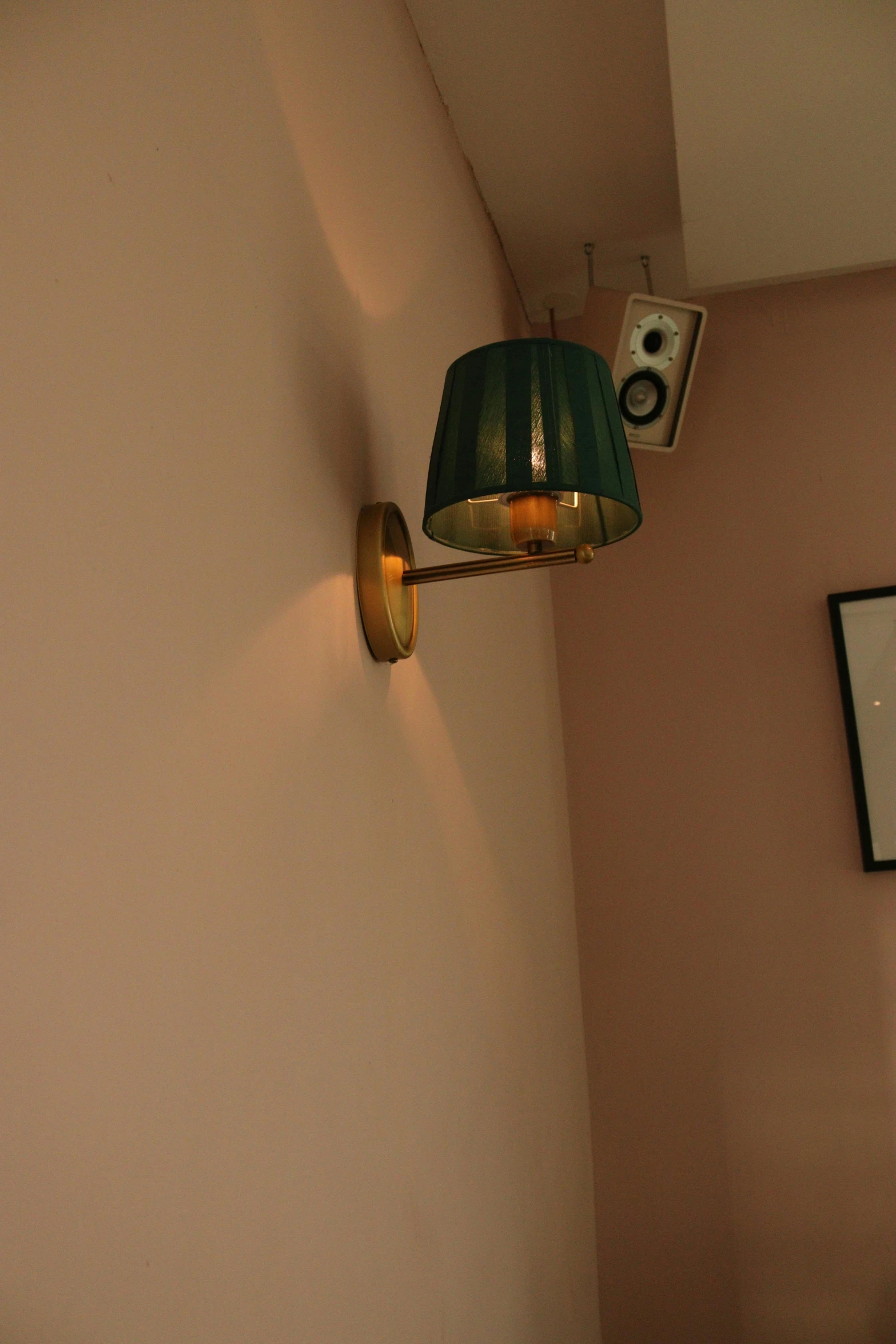 a wall lamp with a green shade next to a white picture on the wall