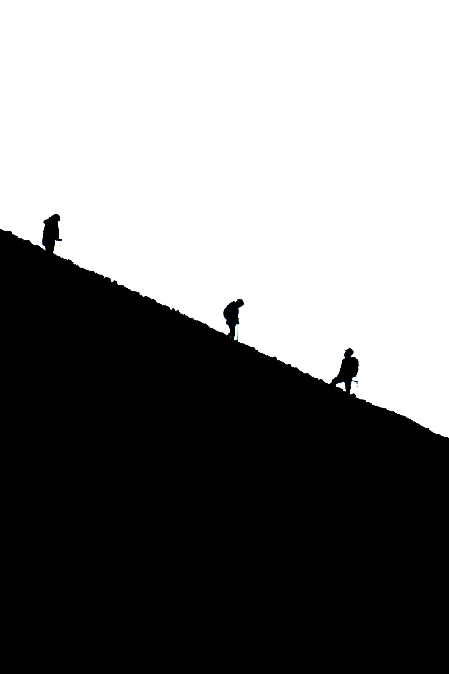 three people climbing up a hill with a snowboard