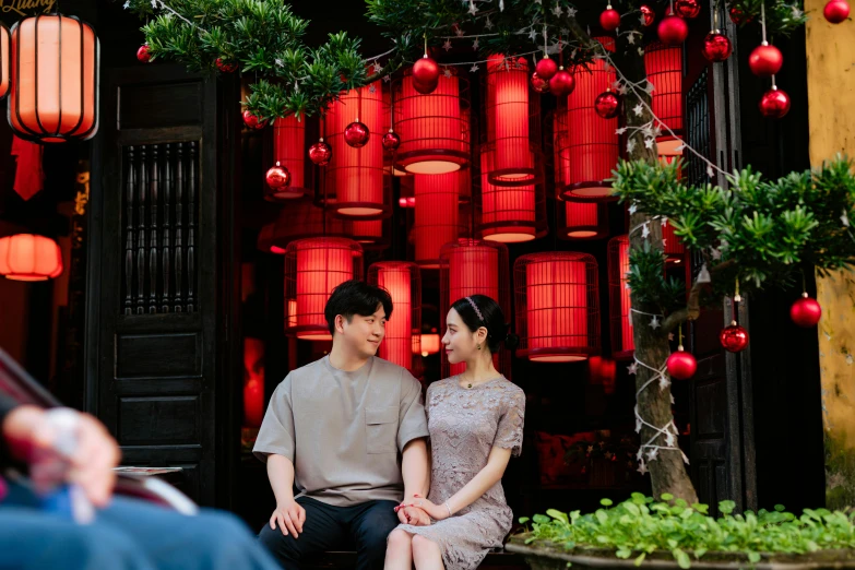 a man and a woman sit close to each other under red lanterns