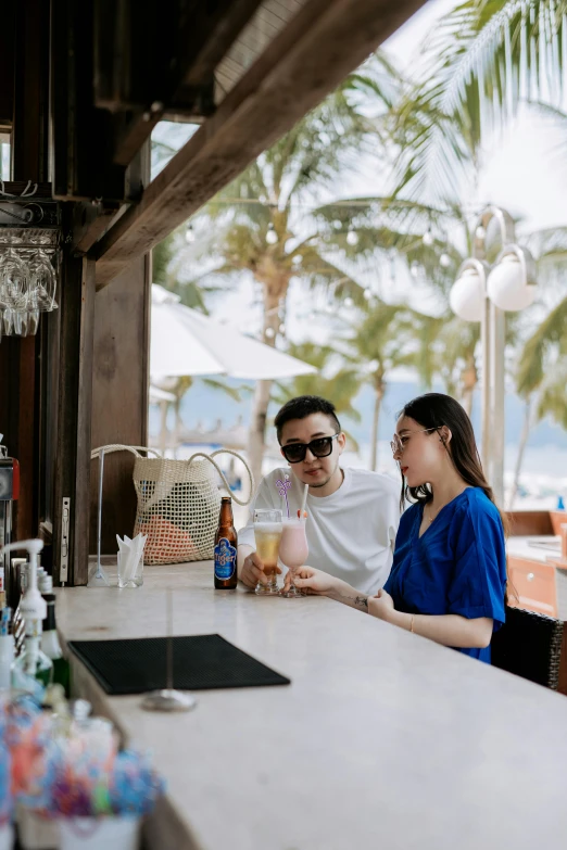 a woman sitting at a table next to a man holding a drink