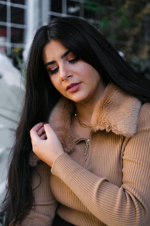 woman standing next to building wearing an open tan sweater and black skirt