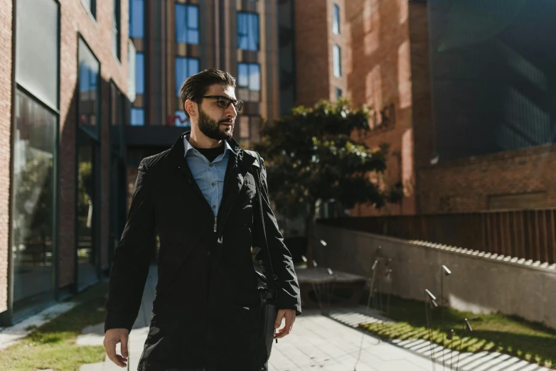 man in glasses walks down the sidewalk near an apartment building