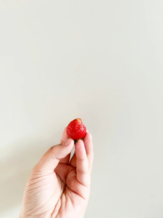 the hand is holding a strawberry on the wall