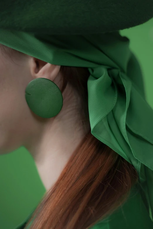 a woman in green wears large round earring with circular design