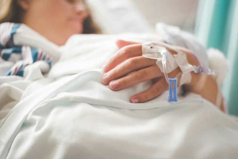 the hands of a person in bed with an iv device