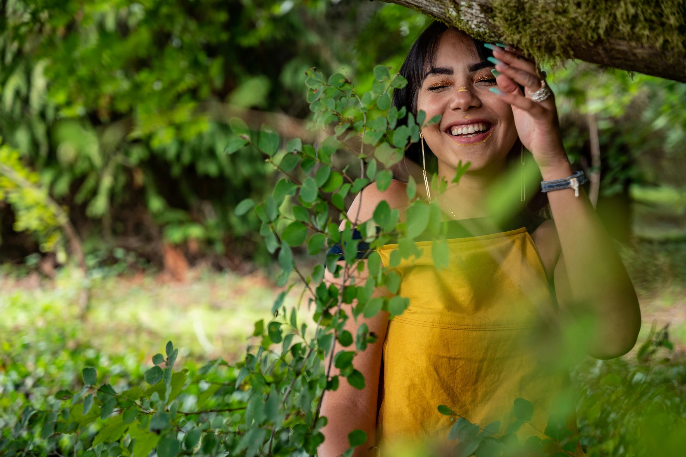 a woman wearing a yellow dress smiling in a forest