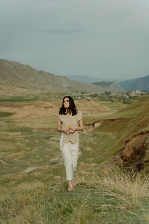 woman with flowers in hand standing near grassy valley