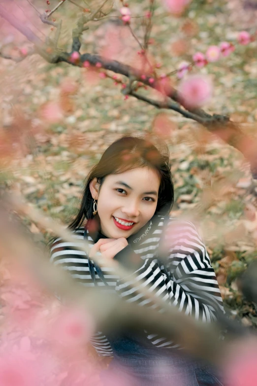 a young woman posing for a pograph under a tree filled with blossoms