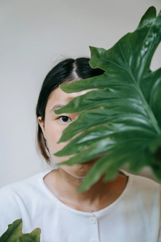 a girl in a white sweater is hiding behind some leaves