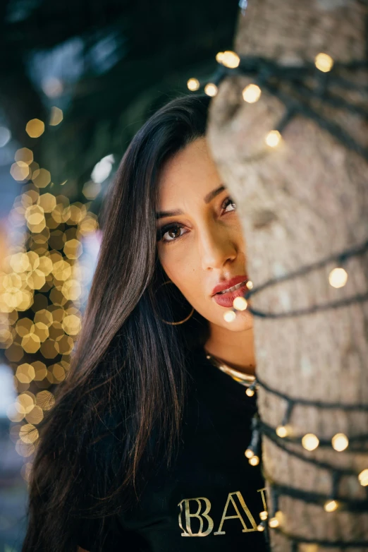 a woman poses near a tree with lights