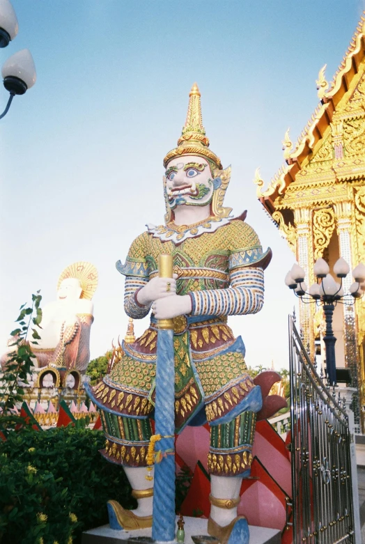 a statue of an asian warrior stands between a row of colorfully designed structures