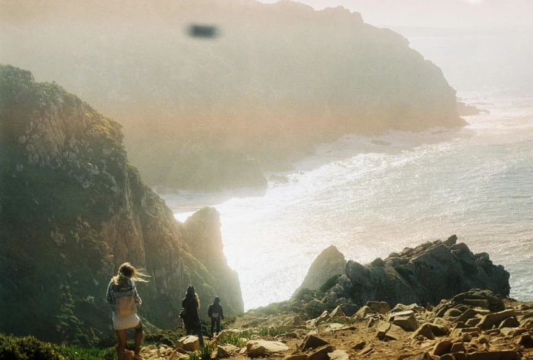 people stand on a steep hill overlooking the ocean