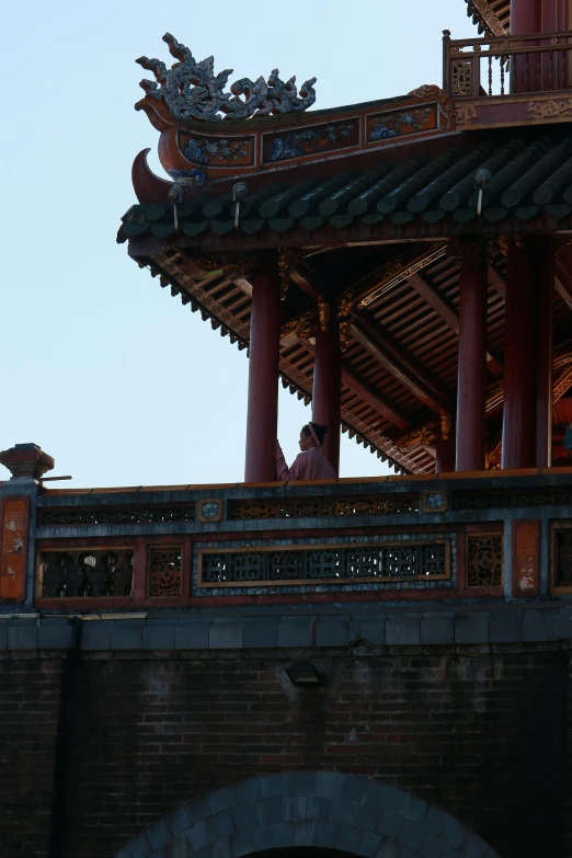 a tall, elaborate chinese building with a man sitting in the upper balcony