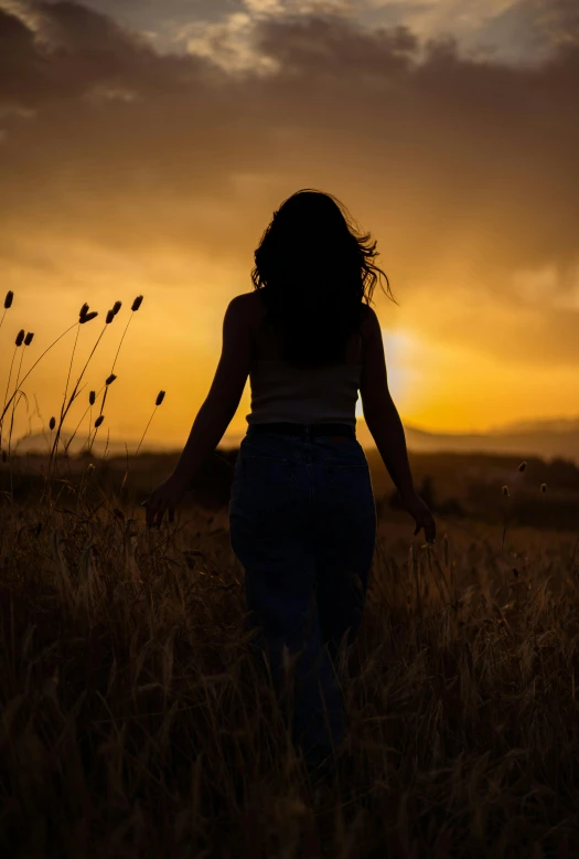 a woman standing in a field at sunset with her back to the camera