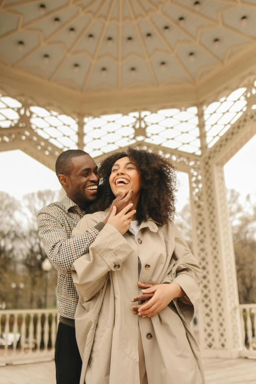 a man and woman laughing while posing in front of a gazebo