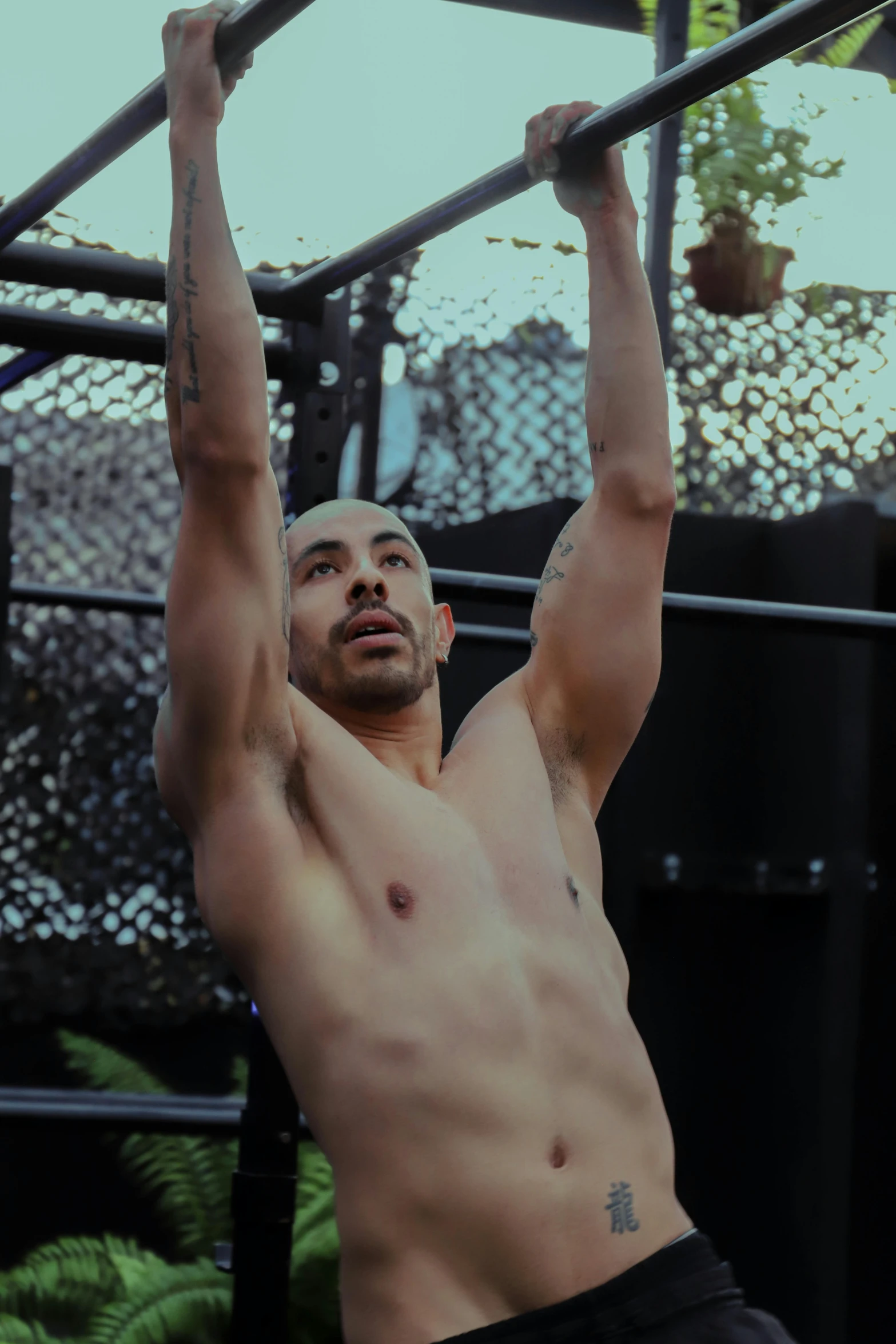 shirtless man holding up a bar with one arm and lifting his hands