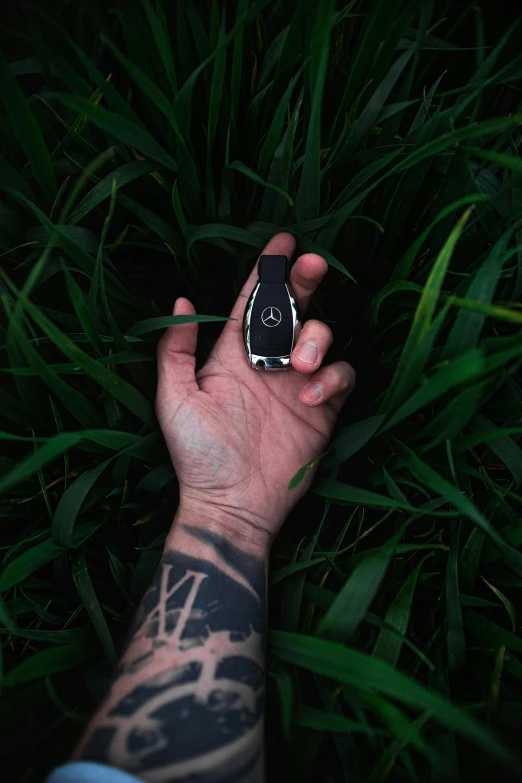 a tattooed hand holding a black cellphone over some grass