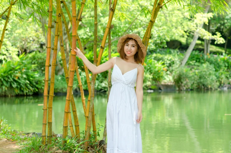 a beautiful woman in white dress posing by a bamboo tree