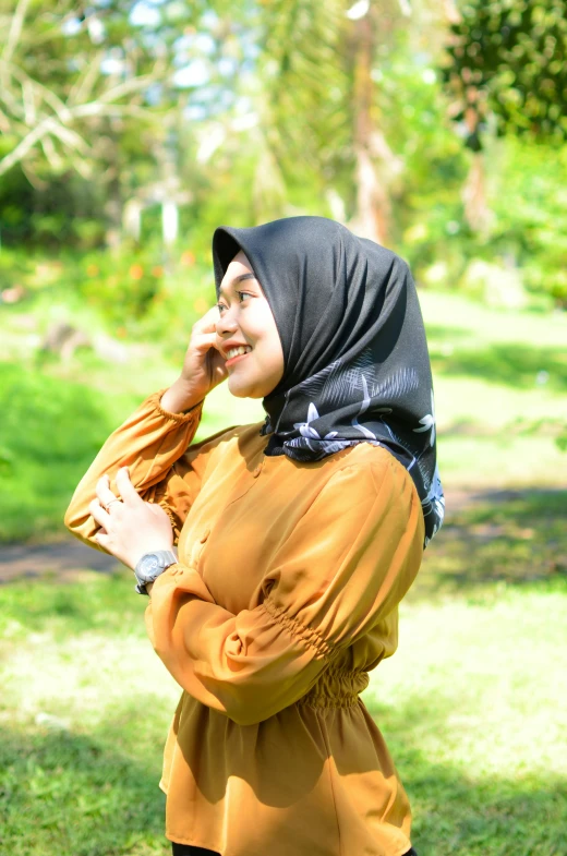 a woman wearing a black headscarf stands near some trees