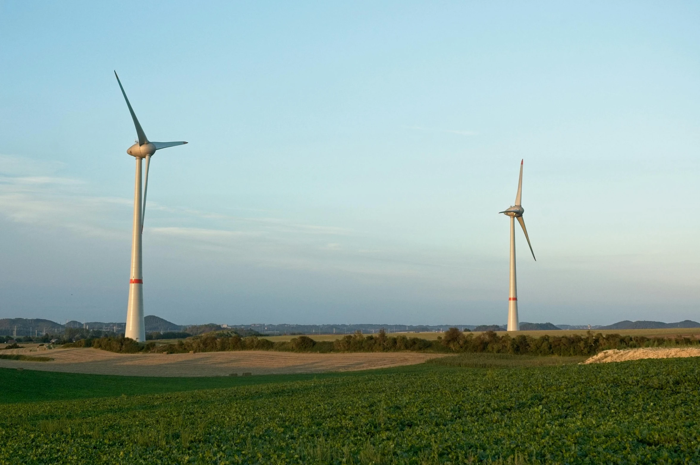 three wind mills, one in the process of being turned down, are in a rural setting