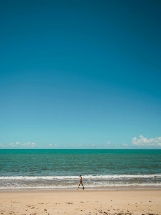 a person walks on the beach while flying a kite