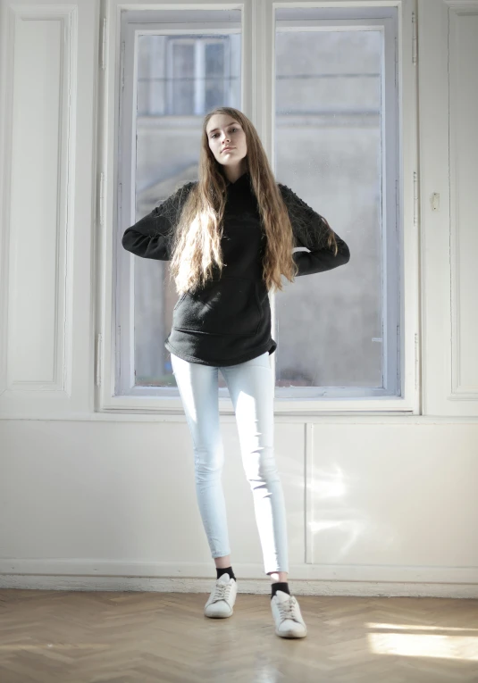 a girl standing by a window with her long hair blowing in the wind