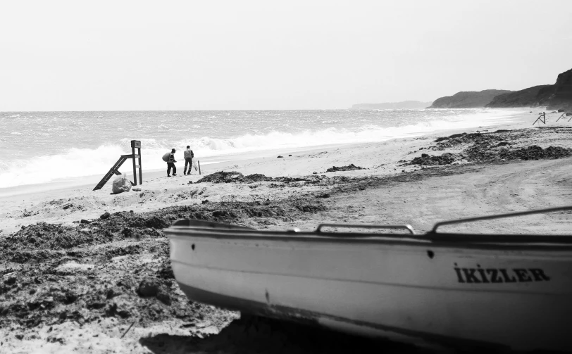 two people walking away from the water with a boat on the beach