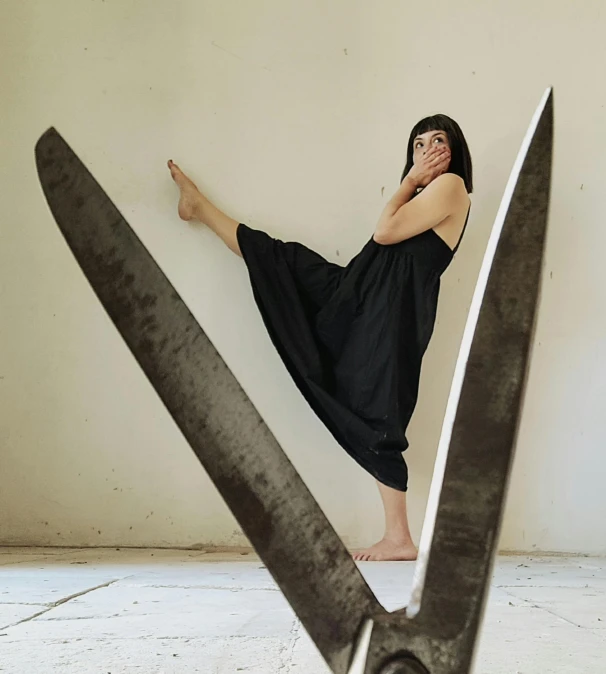 a woman in black dress standing next to a pair of scissors