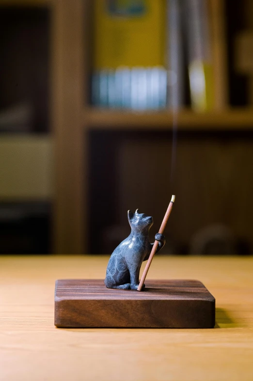 small cat sitting on a wooden base while holding a cigarette