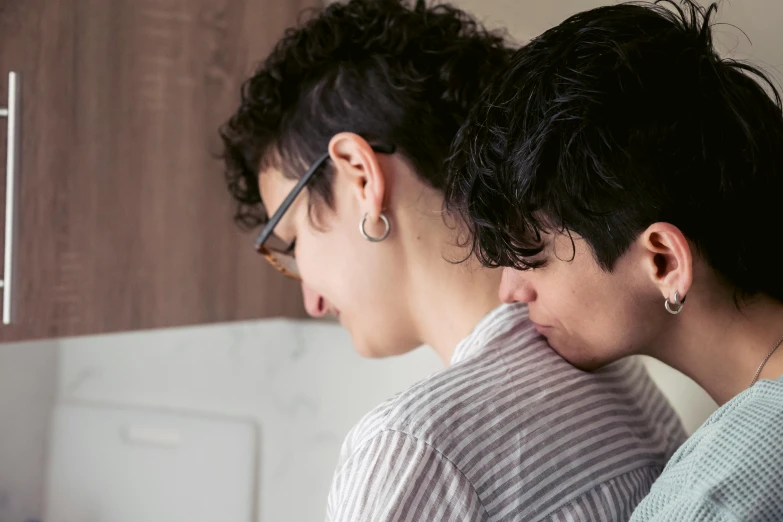 two people standing by each other in front of a wall